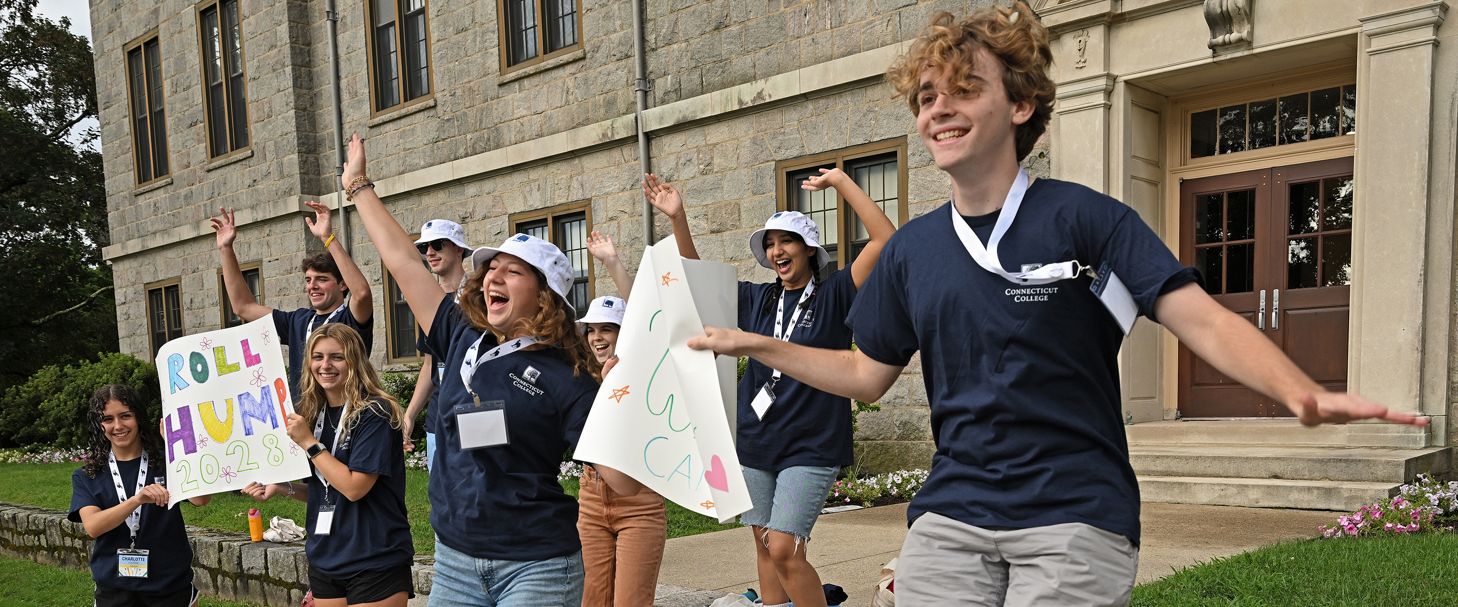 A group of students jump and cheer greeting newcomers to campus